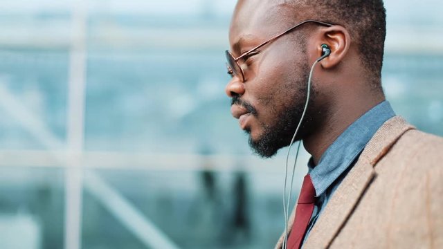 African American businessman listens to the music and dances while he walks near the office building with a smartphone. Concept: office worker, rest, advertising