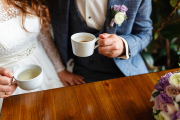 Young couple in a cafe in the attic drinking coffee and tea, sitting. Morning breakfast at the hotel. Cropped image of couple in love holding hands on wooden table while drinking coffee.