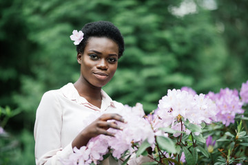 Young black woman with afro hairstyle in urban park. Afro american girl wearing casual clothes between purple flowers.