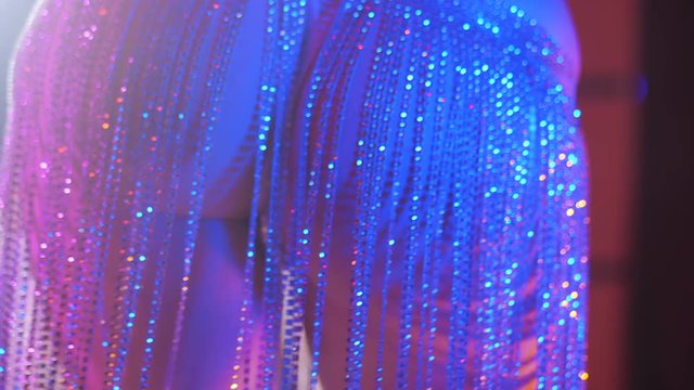 Sexy woman in rhinestones costume. Fringe skirt with pendants made of stones dressed on panties. Striptease dancer moving buttocks on stage in night club with pylone.