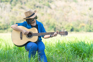 Women short hair wear hat and sunglasses sit playing guitar in grass field