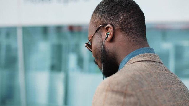 African American businessman listens to the music and dances while he walks near the office building with a smartphone. Concept: office worker, rest, advertising