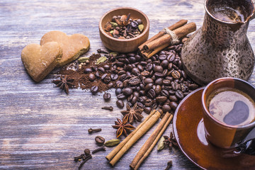 Coffee in a cup, coffee beans, spice, cookies in the shape of heart on a wooden background.