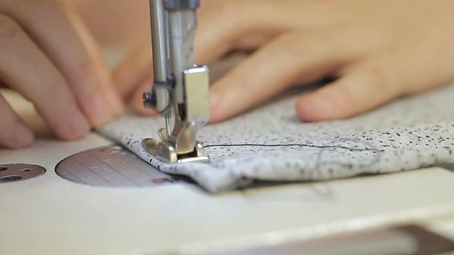Close-up of a hand scribbling cloth on a sewing machine. Female palms support gray material on which automatic device makes an even seam with black thread. After end paw lifts and scissors cut threads