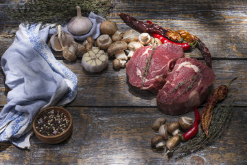 Raw beef steaks, ready for roasting, salt, pepper, tomatoes, garlic on wooden background