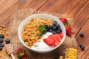 Bowl of homemade granola with yogurt and fresh berries on wooden background