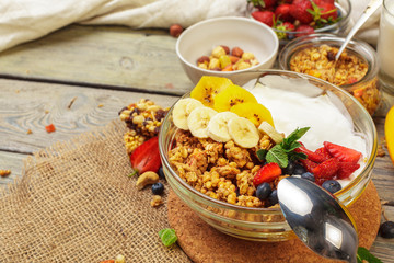 Bowl of homemade granola with yogurt and fresh berries on wooden background
