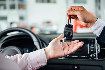 Close photo of male car dealer hand giving a car key to person hand. They are sitting in car.