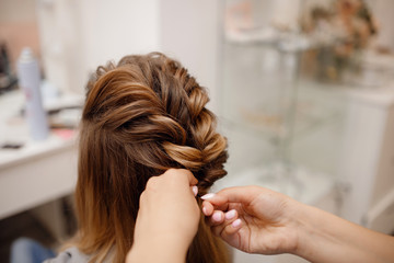 Fototapeta premium Close-up of woman hairdresser weaving plaits in beauty salon.