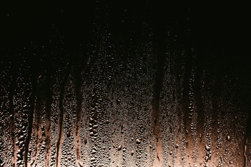 Drops of water flow down the glass at night