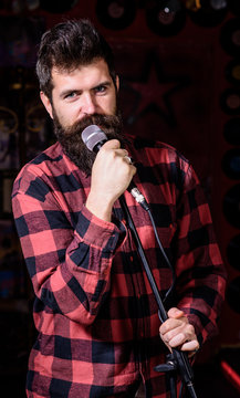 Man with calm face holds microphone, singing song, black background. Guy likes to sing rock songs. Musician with beard and mustache singing song in karaoke. Vocalist concept.
