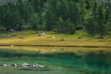 Arpy Lake, Valle d’Aosta, Italy. Alpine pond on Italian alps. Beautiful mountain panorama. Couple enjoying nature in summer day along the pond. Landscape  from Colle San Carlo, La Thuile, IT. 