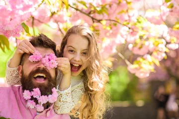 Door stickers Cherryblossom Child and man with tender pink flowers in beard. Girl with dad near sakura flowers on spring day. Father and daughter on happy face play with flowers as glasses, sakura background. Family time concept