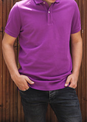 Obraz premium Young Beautiful male model in purple polo T-shirt and dark black and blue jeans on brown wooden background