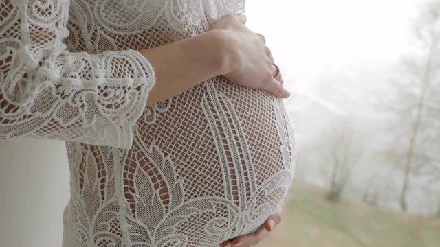beautiful pregnant blonde girl in white knitted dress standing by the big window