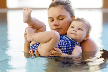 Happy mother swimming with cute adorable baby girl daughter in swimming pool spending spa vacations