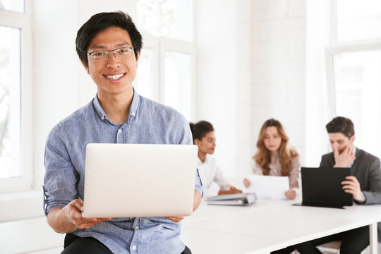 Happy young asian man holding laptop
