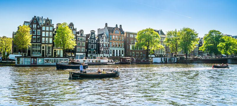 Amsterdam, May 7 2018 - view on the river Amstel filled with small boats and traditional houses in the background on a summer day