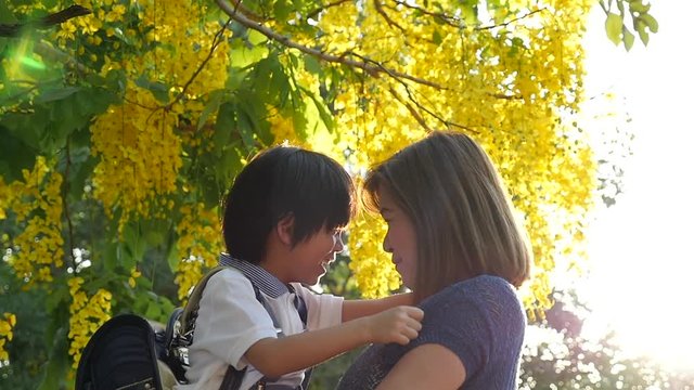 Asian mother holding her son while walking in the park , back to school concept slow motion 