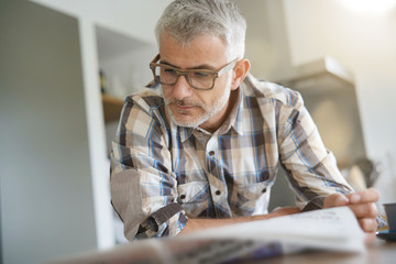 Middle-aged man in kitchen reading newspaper
