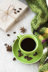 Fresh delicious hot espresso coffee with coffee beans in a green cup and a craft notebook on a light background. Next there is a bright striped plaid.