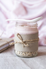 Oatmeal, flavored with yogurt, sprinkled with cinnamon in a glass jar. Next is a craft notebook and a pink napkin.