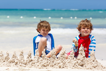 Two little kids boys having fun with building a sand castle on tropical beach of carribean island.