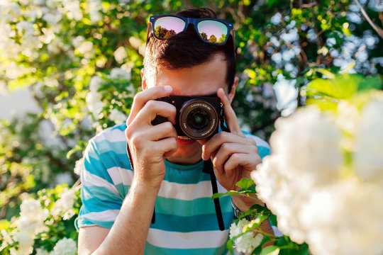 Man photographer taking pictures of flowers in park at sunset. Young guy enjoys his hobby outside. Close-up of camera.