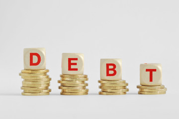 The word debt written with wood blocks on top of coins piles - Debt decrease concept