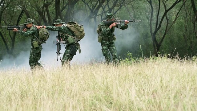 Soldiers aiming their assault rifle in jungle. Chinese soldiers in jungle walking toward camera in open grass land and aiming their weapon, special forces training. Panning shot.