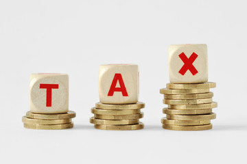 The word Tax written with wood blocks on top of coins piles - Tax increase concept