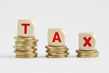 The word Tax written with wood blocks on top of coins piles - Tax decrease concept