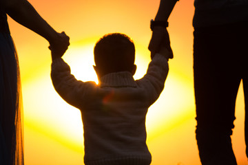The kid is holding hands of parents in the sun