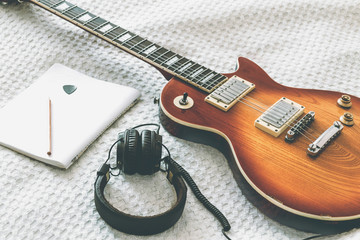 Fototapeta premium The electric guitar is on a white blanket next to the tablet and headphones