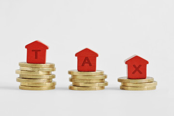 The word Tax written with miniature houses on top of coins - Home taxes decrease concept