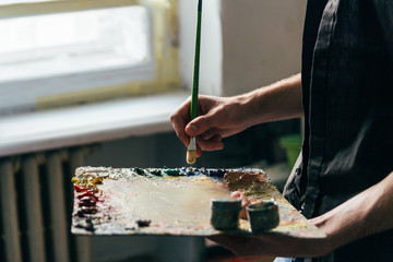 across from the window the artist holds a palette with paints and a brush and is going to paint on...