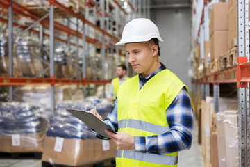 logistic business, shipment and people concept - male worker or supervisor with clipboard in reflective safety vest at warehouse