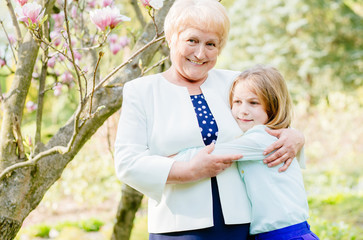 Happy grandmother with granddaughter under blossom tree in garden together.