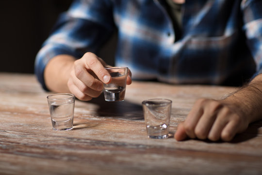 alcoholism, alcohol addiction and people concept - hands of male alcoholic drinking vodka shots at night