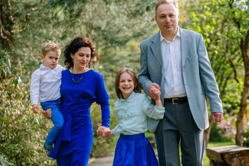 Fototapeta premium Lovely young family of four walking hand in hand in summer park.