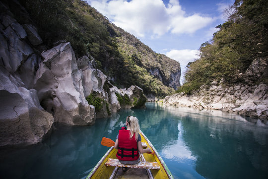 Rear view of woman sitting in boat on river amidst mountains against sky