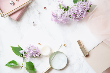 Top vew composition with feminine workspace mock up with lilac flowers and pink accessories on marble background