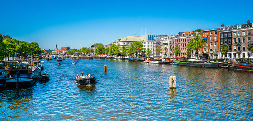 Fototapeta premium Amsterdam, May 7 2018 - view on the river Amstel filled with small boats and the Carre theater in the background on a summer day