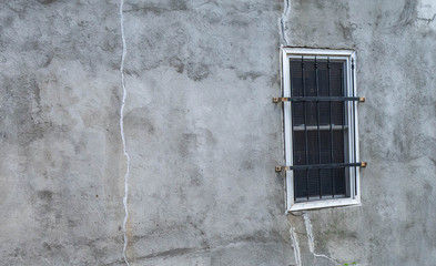 A black and white photo of a stucco wall with a single barred window.