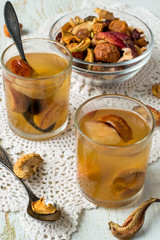 
  A mixture of dried fruits in a small round glass bowl, next to two glasses with compote on an old table. Delicious and healthy drink. 