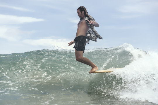 Man surfing while standing on surfboard's edge in sea against sky