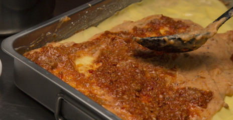 closeup of seasoning lasagne with tomato sauce in a pan
