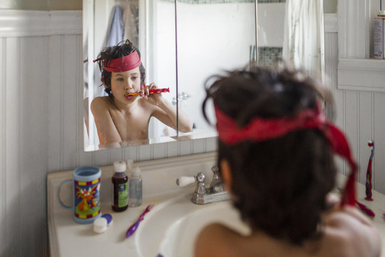 Shirtless boy brushing his teeth in front of mirror in bathroom