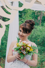 Naklejka premium Beautiful woman in a wedding dress on a photozone decorated with fresh flowers, posing and portrait.