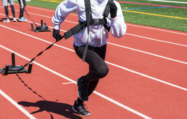 Fototapeta premium High school girls running toward camera pulling a sled with weights